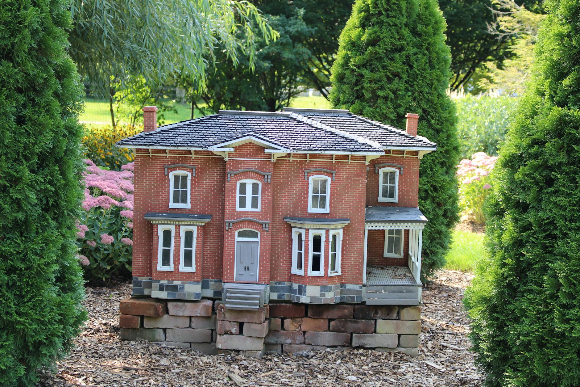Miniaturowy murowany domek letniskowy w otoczeniu ogrodu